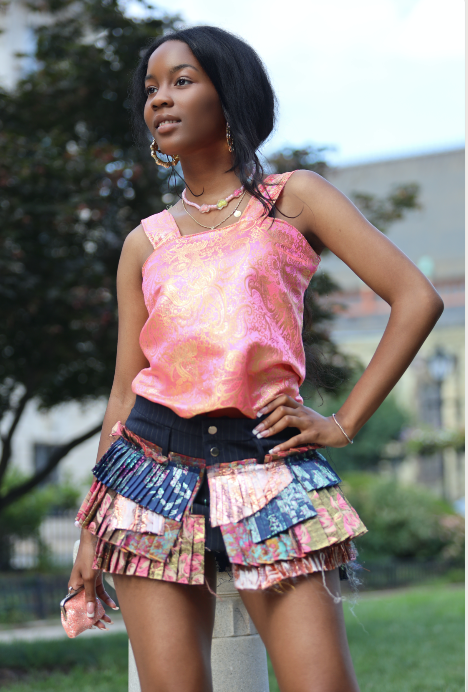 Woman wearing a colorful outfit with a pink top and multicolored skirt outdoors.